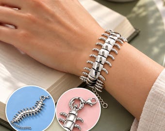 Puede incluir: Una pulsera plateada con forma de ciempiés, con partes del cuerpo segmentadas y múltiples patas pequeñas. La pulsera cuenta con un cierre de mosquetón y una cadena de extensión ajustable, mostrada en una muñeca y en dos recuadros circulares.