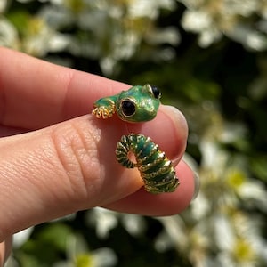 May include: A gold-toned wrap ring featuring a green enameled frog head with black eyes at one end and a green enameled caterpillar body with gold segmented detailing at the other end, designed to wrap around the finger in an open-ended style.