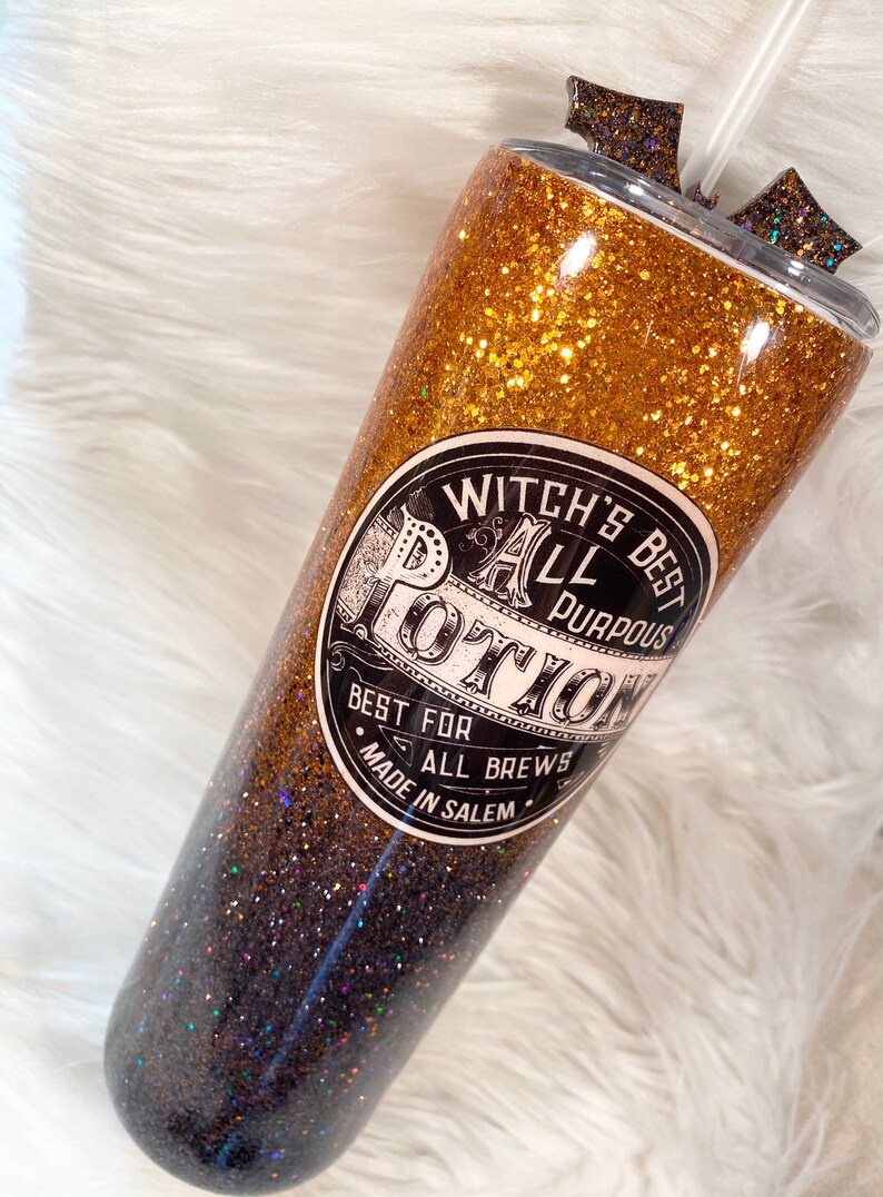 May include: Glittery tumbler with a gold and black ombre design. The tumbler features a label that reads "Witch's Best All Purpous Potion, Best for All Brews, Made in Salem". Includes a straw and decorative accents.