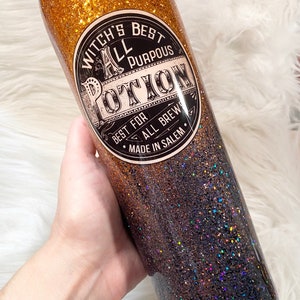 May include: A glitter-covered tumbler with a gradient of gold to dark blue. The tumbler features a circular label with the text "Witch's Best All Purpous Potion" and "Best for All Brews Made in Salem."