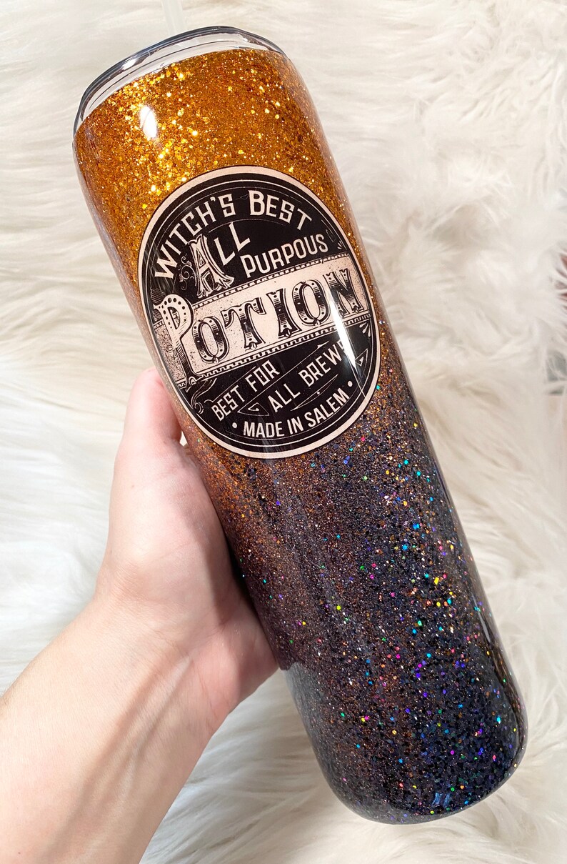 May include: A glitter-covered tumbler with a gradient of gold to dark blue. The tumbler features a circular label with the text "Witch's Best All Purpous Potion" and "Best for All Brews Made in Salem."