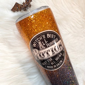 May include: A glittery tumbler with a bat-shaped topper. The tumbler is gold and black with the text "Witch's Best All Purpous Potion" on the front. The tumbler is made in Salem.