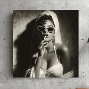 Könnte beinhalten: Schwarz-Weiß-Druck einer Frau mit Sonnenbrille und Handtuch, die eine Zigarette raucht. Das Kunstwerk hängt an einer Betonwand, davor ein grauer Sessel und hölzerne Beistelltische. Ein kleines gerahmtes Schild ist links zu sehen.
