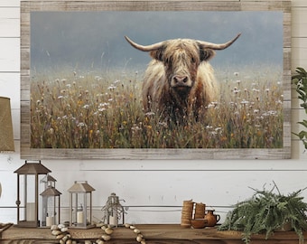 May include: A framed canvas print of a Highland cow standing in a field of wildflowers. The cow has long, shaggy, light brown fur and large horns. The artwork is set against a soft, hazy background, and framed in a rustic wooden frame.