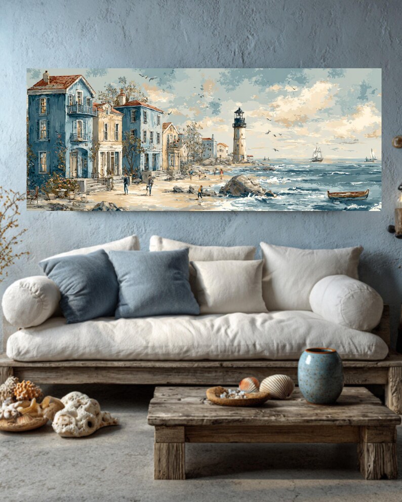 May include: Coastal landscape painting featuring a seaside town with blue buildings, a lighthouse, and a sailboat on the ocean. The artwork has a vintage aesthetic with muted colors and a serene atmosphere. The painting is displayed above a wooden sofa with pillows.
