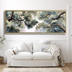 May include: A framed artwork depicting a view of tree branches and foliage from below. The painting features a gold frame and a color palette of greens, blues, and whites. The artwork hangs above a white sofa with pillows and a blanket.