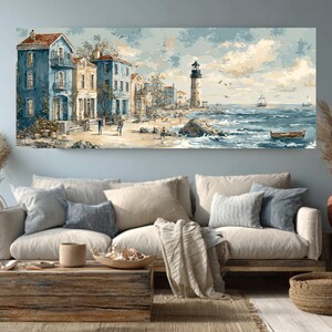 May include: A coastal landscape painting depicts buildings in shades of blue and yellow along a beach, with a lighthouse in the distance. The artwork features a serene ocean with small boats and a cloudy sky. The painting is displayed above a beige sofa with decorative pillows.
