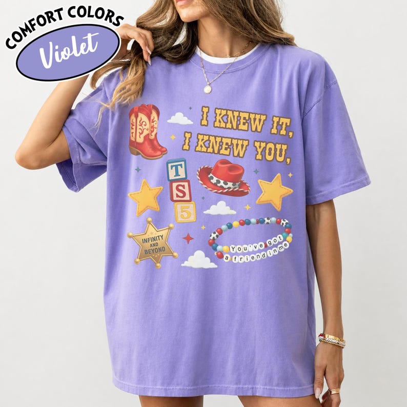 May include: A violet short-sleeve t-shirt featuring a graphic print with the text I KNEW IT, I KNEW YOU, a red cowboy boot, a red cowboy hat, alphabet blocks with TS5, yellow stars, a sheriff badge with INFINITY AND BEYOND, and a beaded bracelet.