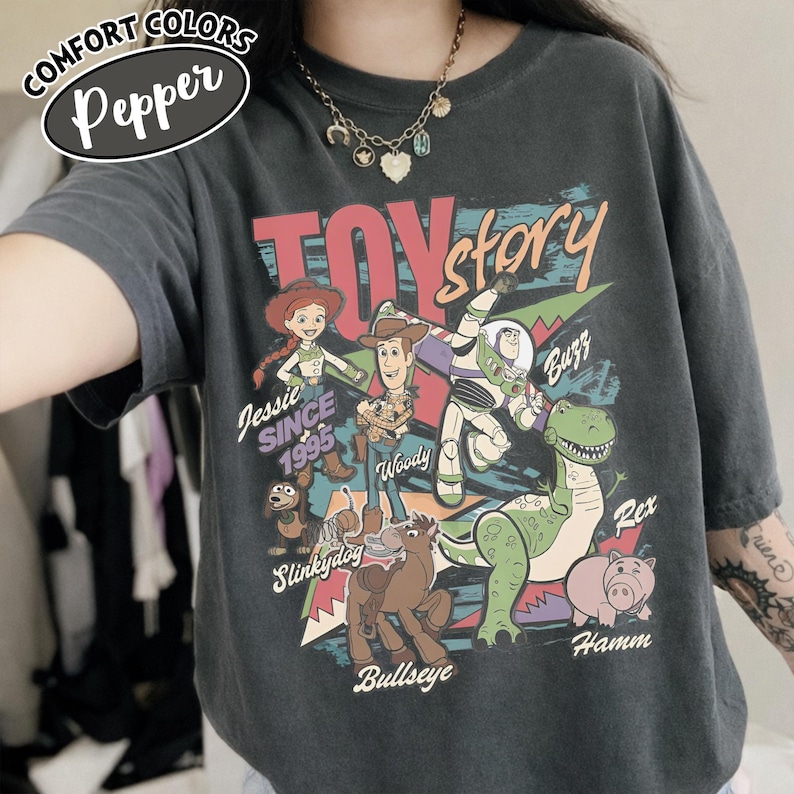 May include: Dark gray Comfort Colors t-shirt featuring a Toy Story graphic. The design includes characters like Woody, Buzz Lightyear, and Rex, with the text "Toy Story" and "Jessie Since 1995".