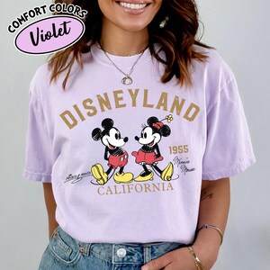 K&ouml;nnte beinhalten: Ein violettes Comfort Colors T-Shirt mit einem Disneyland-Motiv. Das Design zeigt Micky und Minnie Maus, den Text "Disneyland 1955 California" und die Unterschriften "Mickey Mouse" und "Minnie Mouse".