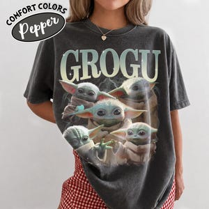 May include: Dark gray t-shirt featuring the word "GROGU" in large, light green letters. Below the text are multiple images of Grogu, the character from The Mandalorian. The shirt has the words "COMFORT COLORS" and "Pepper" in a white oval.