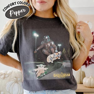 May include: Dark gray Comfort Colors t-shirt featuring a graphic of The Mandalorian and Grogu skateboarding at night. The text "THE MANDALORIAN...THIS IS THE WAY" is printed below the image. The shirt has a Pepper color.