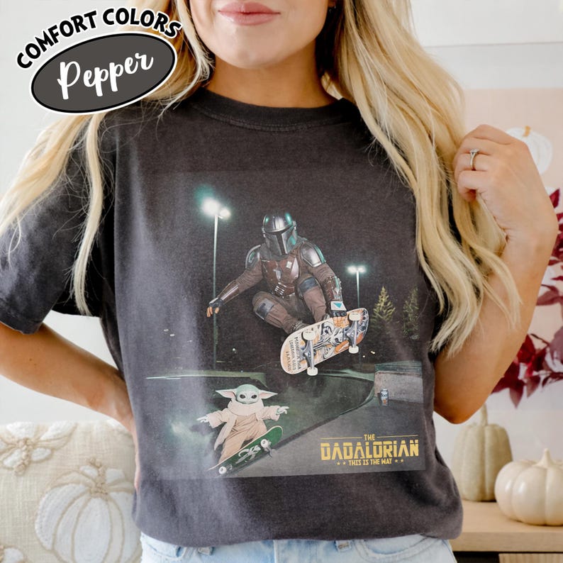 May include: Dark gray Comfort Colors t-shirt featuring a graphic of The Mandalorian and Grogu skateboarding at night. The text "THE MANDALORIAN...THIS IS THE WAY" is printed below the image. The shirt has a Pepper color.