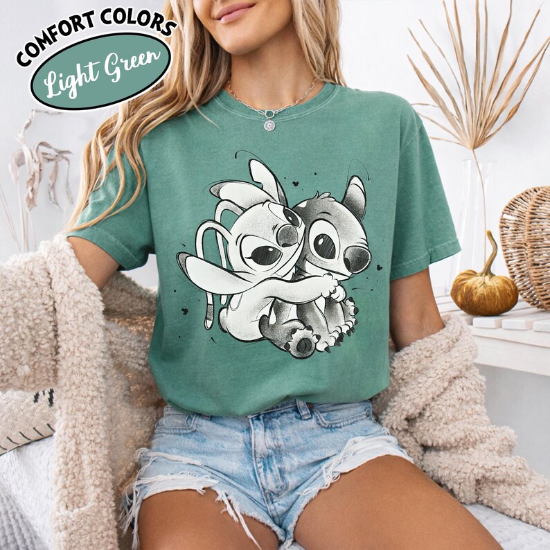 May include: Light green t-shirt featuring a graphic of two cartoon characters hugging. The shirt has the words "Comfort Colors" and "Light Green" in a circular design. The shirt is short-sleeved and made of a soft material.
