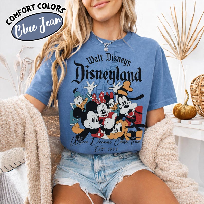 May include: Blue t-shirt with the text "Walt Disney's Disneyland" and a graphic of Mickey Mouse, Minnie Mouse, Donald Duck, Goofy, and Pluto. The shirt also has the text "Where Dreams Come True" and "Est. 1955".