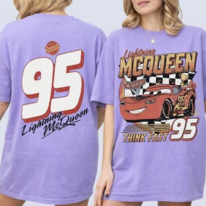 May include: Lavender t-shirts featuring Lightning McQueen from the Cars film. One shirt displays a large "95" with "Lightning McQueen" text. The other shirt has a graphic of McQueen with "Lightning McQueen" and "Think Fast" text.