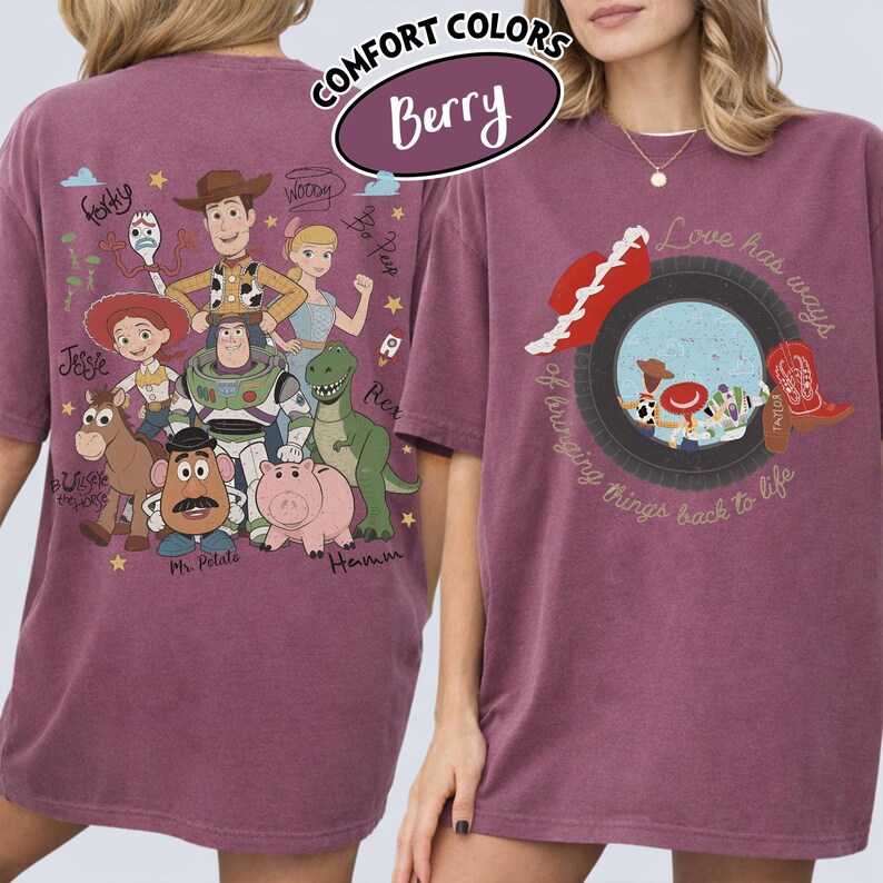 May include: A berry-colored t-shirt featuring Toy Story characters on the back, including Woody, Buzz Lightyear, Jessie, and Rex, with their names written nearby. The front displays a tire graphic with a cowboy hat, boot, and the text Love has ways of bringing things back to life.