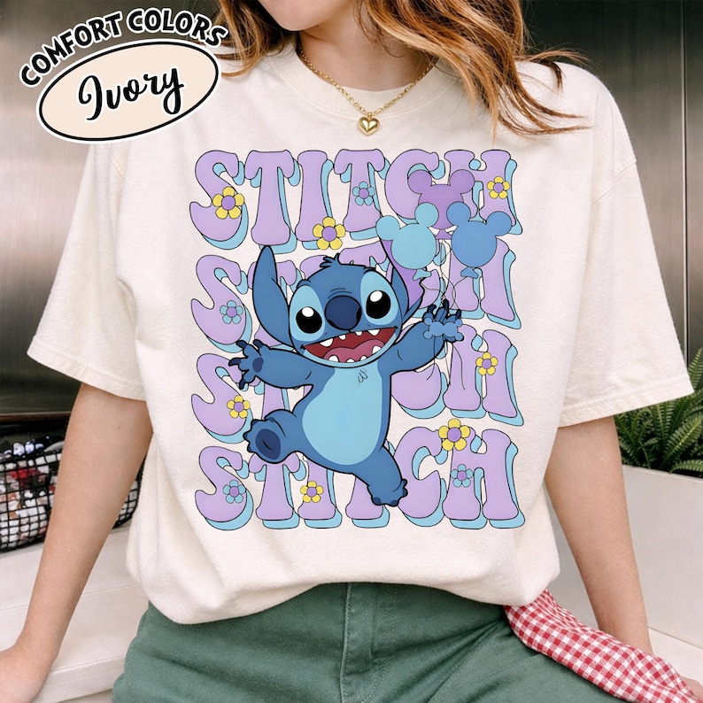 Puede incluir: Camiseta de color marfil con un dise&ntilde;o retro que presenta la palabra "Stitch" y un personaje de dibujos animados. El dise&ntilde;o incluye a Stitch, flores y globos con forma de Mickey Mouse en tonos azules y morados. La camiseta tiene mangas cortas.