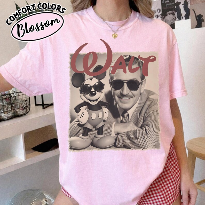 May include: Light pink t-shirt featuring a graphic of Mickey Mouse wearing sunglasses next to a black and white image of Walt Disney. The word "WALT" is printed above the images in a burgundy color. The shirt has the words "Comfort Colors Blossom" printed on the top left.