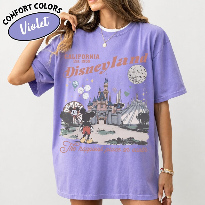 May include: Violet Comfort Colors t-shirt featuring a Disneyland graphic. The design includes a castle, Mickey Mouse, and the text "California Disneyland Est. 1955" and "The happiest place on earth."