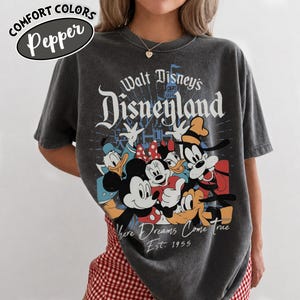 May include: Dark gray Comfort Colors t-shirt featuring a graphic of Disney characters including Mickey Mouse, Minnie Mouse, Donald Duck, and Goofy. The shirt has the text "Walt Disney's Disneyland" and "Where Dreams Come True Est. 1955".