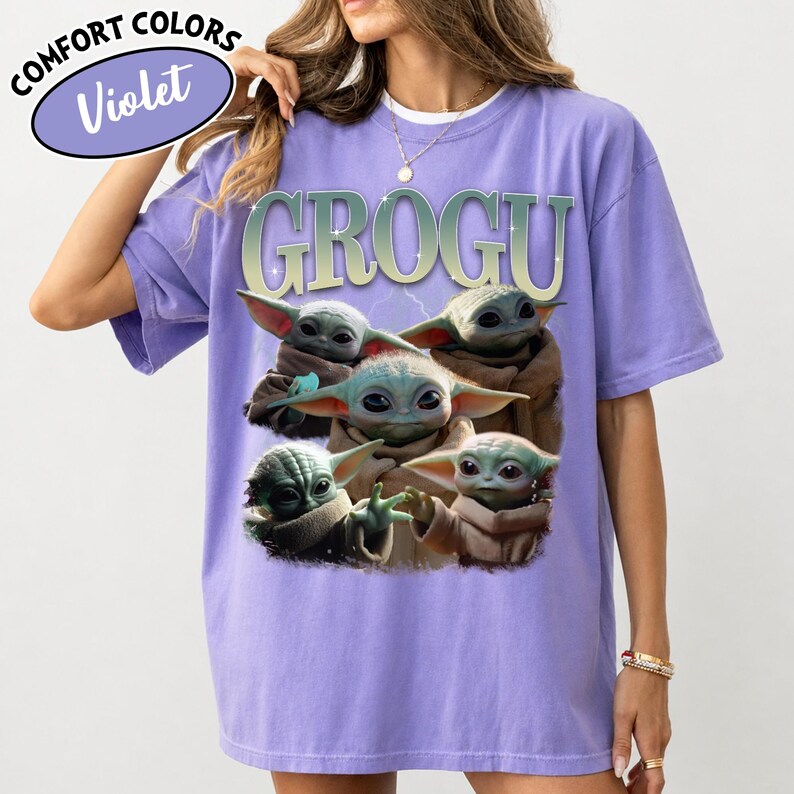 May include: Violet Comfort Colors t-shirt featuring a graphic of Grogu, also known as Baby Yoda, with the word "GROGU" in a green and white font. The shirt has a relaxed fit and short sleeves.