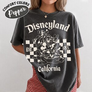 May include: Dark gray t-shirt with a Disneyland graphic. The design features Mickey Mouse, Donald Duck, Goofy, and Minnie Mouse, with the text "Disneyland California 1955". The shirt has a vintage, worn look.