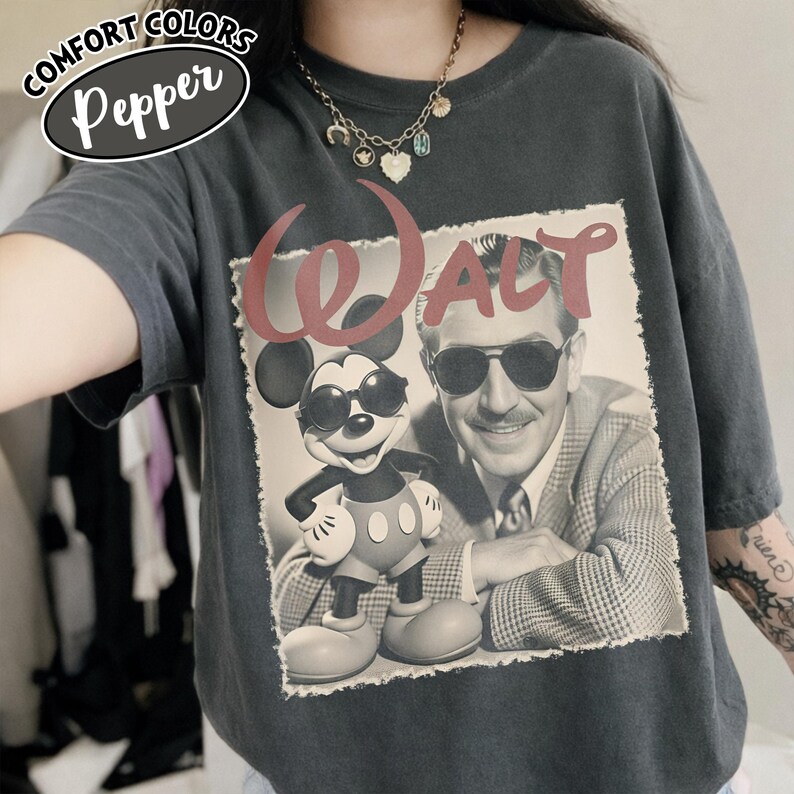May include: Dark gray Comfort Colors t-shirt with a graphic featuring Mickey Mouse wearing sunglasses and Walt Disney. The word "WALT" is printed in red above the image. The shirt has a relaxed fit.