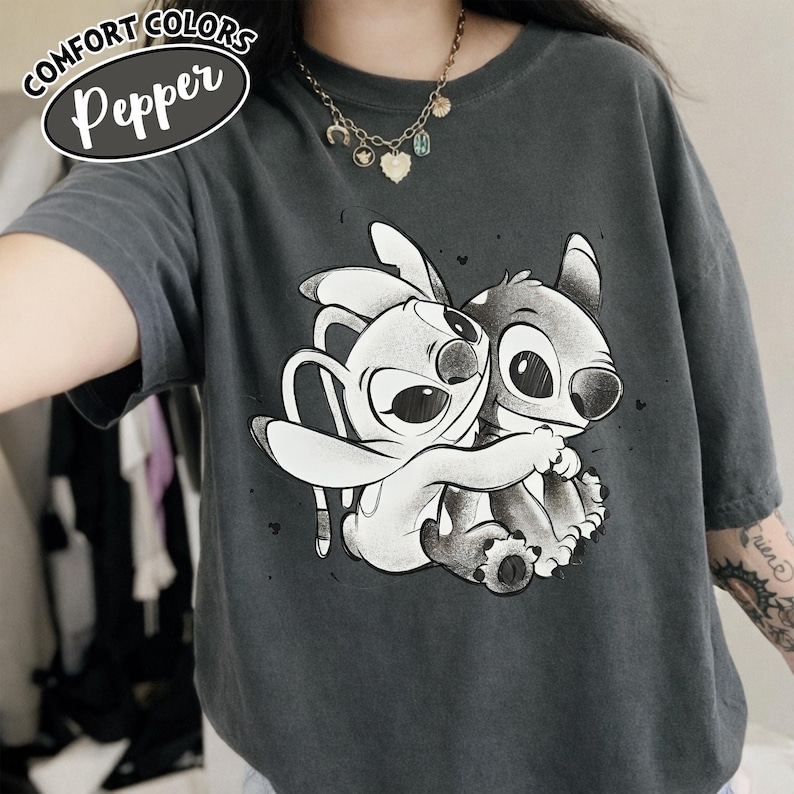 May include: Dark gray Comfort Colors Pepper t-shirt featuring a graphic of two cartoon characters hugging. The shirt has short sleeves and a crew neck. The text "COMFORT COLORS" and "Pepper" are printed on the top left of the shirt.