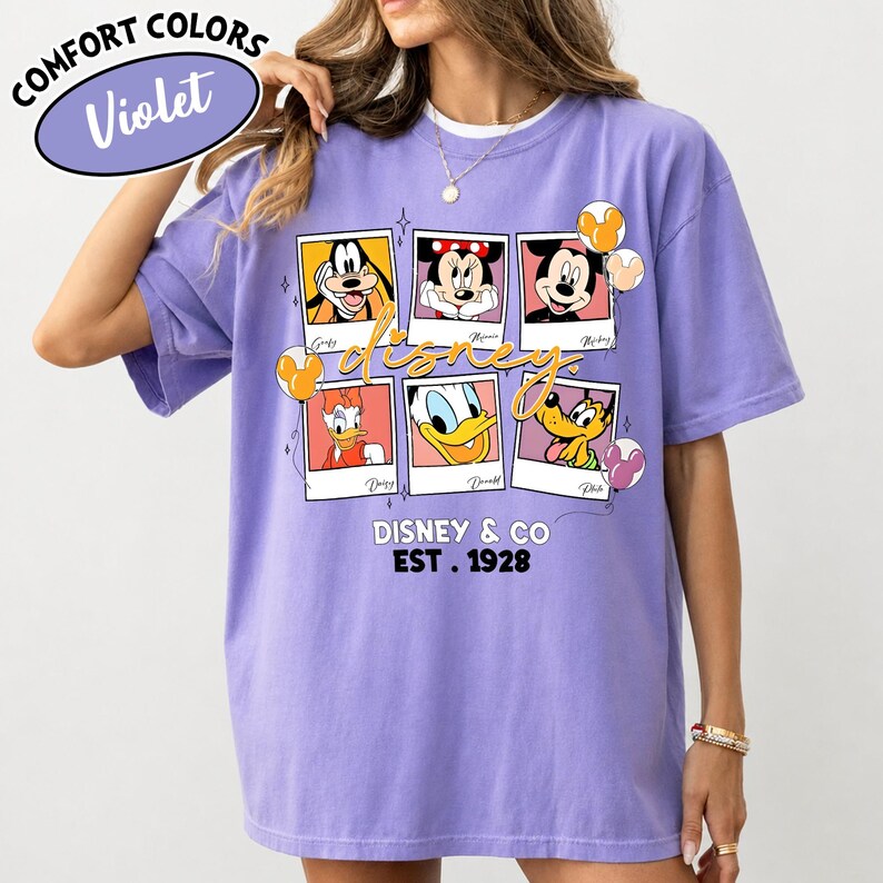 Op de afbeelding: Violet Comfort Colors T-shirt met een Disney-ontwerp. Het ontwerp bevat afbeeldingen van Disney-personages zoals Mickey Mouse, Minnie Mouse, Donald Duck en Goofy. Het shirt heeft ook de tekst "Disney & Co. Est. 1928".