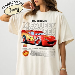 May include: Ivory-colored t-shirt featuring a graphic of the character Lightning McQueen from the movie Cars. The design includes the text "EL RAYO MCQUEEN" and "95". The shirt also has the "Rusteze" logo.