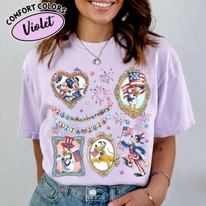 May include: A violet Comfort Colors t-shirt featuring framed cartoon characters in patriotic attire. The shirt includes Mickey and Minnie Mouse, Donald Duck, Pluto, and Goofy, with fireworks and the text "250th Anniversary 1776-2026."