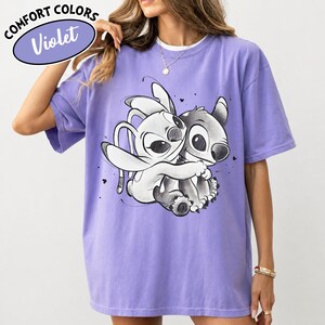 May include: Violet Comfort Colors t-shirt featuring a black and white graphic of two cartoon characters embracing. The shirt has short sleeves and a crew neck. The text "COMFORT COLORS" and "Violet" are in a purple oval on the top left.