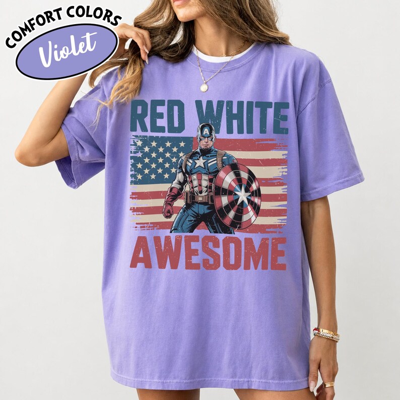 K&ouml;nnte beinhalten: Violettes Comfort Colors T-Shirt mit Captain America und dem Text "RED WHITE AWESOME" &uuml;ber einem abgenutzten amerikanischen Flaggen-Design. Das Shirt hat kurze &Auml;rmel und einen Rundhalsausschnitt.
