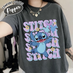 Puede incluir: Camiseta Comfort Colors gris oscuro con la palabra "Stitch" repetida verticalmente en una fuente retro, y un personaje de dibujos animados Stitch sosteniendo globos. La camiseta tambi&eacute;n tiene la palabra "Pepper" en un &oacute;valo blanco.