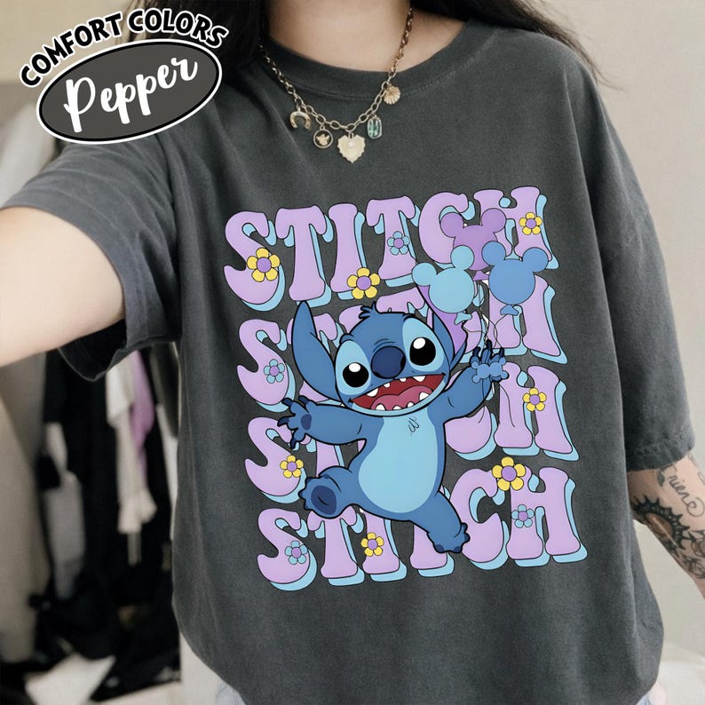 Puede incluir: Camiseta Comfort Colors gris oscuro con la palabra "Stitch" repetida verticalmente en una fuente retro, y un personaje de dibujos animados Stitch sosteniendo globos. La camiseta tambi&eacute;n tiene la palabra "Pepper" en un &oacute;valo blanco.