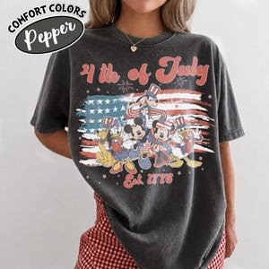 May include: Dark gray t-shirt with a distressed graphic featuring Disney characters in patriotic attire in front of an American flag. The text "4th of July" and "Est. 1776" are also displayed.