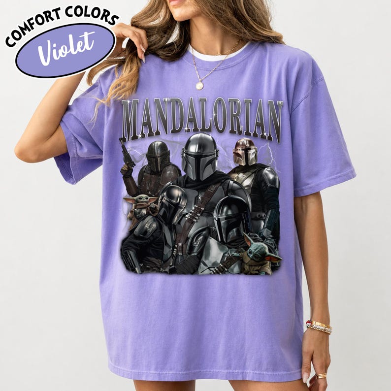 Puede incluir: Camiseta violeta Comfort Colors con un gr&aacute;fico de personajes de Mandalorian. La palabra "MANDALORIAN" est&aacute; impresa en la parte superior. La camiseta tiene cuello redondo y mangas cortas.