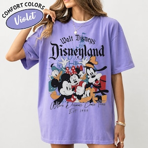 May include: Violet Comfort Colors t-shirt featuring a graphic of Disney characters including Mickey Mouse, Minnie Mouse, Donald Duck, and Goofy. The shirt has the text "Walt Disney's Disneyland" and "Where Dreams Come True Est. 1955".