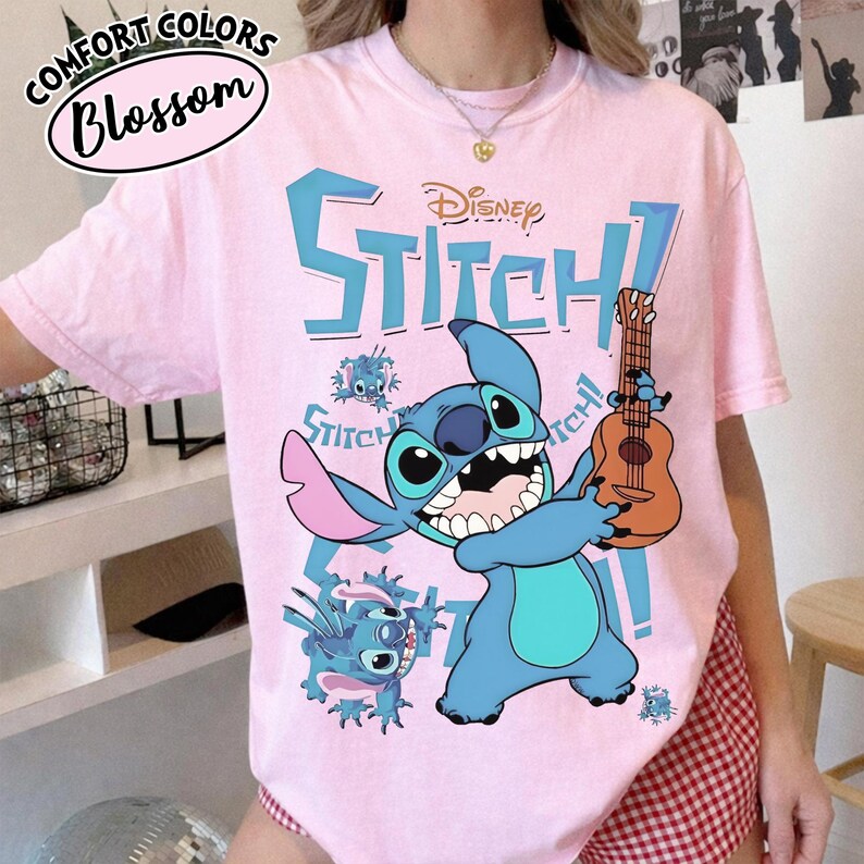 Pu&ograve; includere: T-shirt rosa chiaro con il personaggio Disney Stitch che tiene un ukulele. La parola "Stitch!" &egrave; stampata in blu, con il logo Disney sopra. La maglietta ha anche le parole "Comfort Colors" e "Blossom".