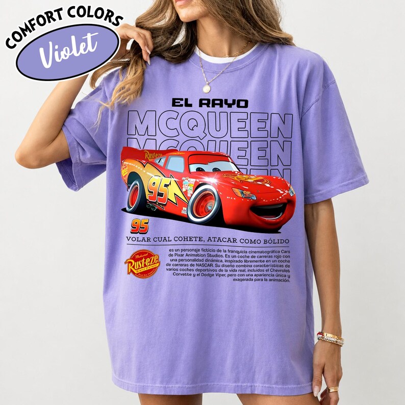 May include: Violet Comfort Colors t-shirt featuring a graphic of Lightning McQueen from the movie Cars. The design includes the text "EL RAYO MCQUEEN" and "95". The shirt also has text in Spanish.
