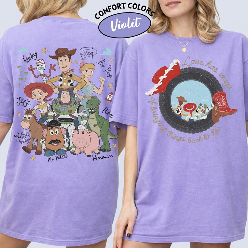 May include: A light purple t-shirt featuring a graphic of Toy Story characters on the back and a tire graphic with a cowboy hat and boot on the front. The back includes text labels for Forky, Woody, Bo Peep, Jessie, Rex, Bullseye, Mr. Potato, and Hamm.