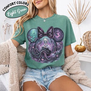 May include: Light green t-shirt featuring a graphic of Ursula from The Little Mermaid, designed in the shape of Mickey Mouse ears. The design includes a purple bow, sea elements, and the text "Comfort Colors Light Green".