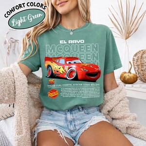 May include: Light green t-shirt featuring a graphic of Lightning McQueen from the movie Cars. The design includes the text "EL RAYO MCQUEEN" and "95". The shirt also has the text "VOLAR CUAL COHETE, ATACAR COMO B&Oacute;LIDO" and the Rust-eze logo.