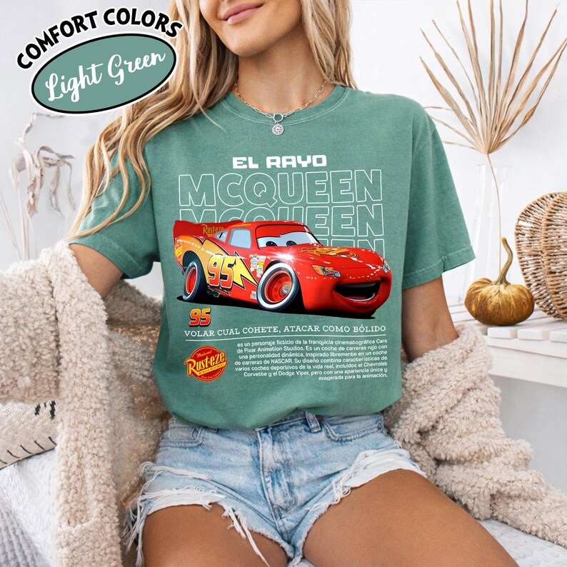 May include: Light green t-shirt featuring a graphic of Lightning McQueen from the movie Cars. The design includes the text "EL RAYO MCQUEEN" and "95". The shirt also has the text "VOLAR CUAL COHETE, ATACAR COMO B&Oacute;LIDO" and the Rust-eze logo.