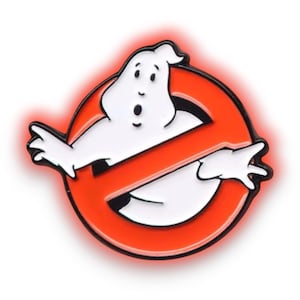 May include: A pin badge of the Ghostbusters logo. The design features a white ghost inside a red circle with a red diagonal line. The badge has a black border and a red glow effect.
