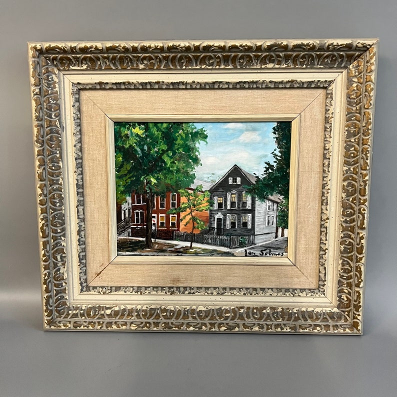 May include: Framed painting of a street scene with three houses. The houses are painted in shades of gray, red, and orange. The painting is signed "Jon Simes" in the bottom right corner.