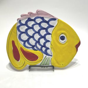 May include: A ceramic fish-shaped plate with a yellow body, blue and white scales, red and green accents, and a pink fin.