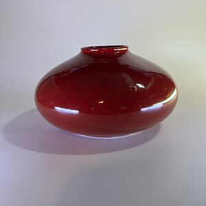 May include: A deep red ceramic vase with a rounded, bulbous shape. The vase has a smooth, glossy finish.
