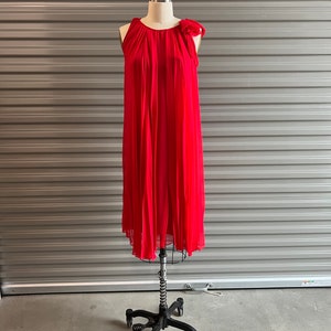 Può includere: Un abito rosso senza maniche con gonna plissettata e un dettaglio a fiocco sulla spalla.